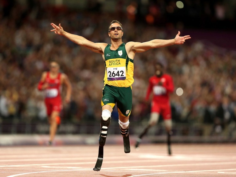 Định mệnh đã lấy đi của Oscar Pistorius đôi chân, khiến anh phải sống đời tàn tật từ khi cất tiếng khóc lọt lòng. Nhưng từ sâu thẳm trái tim mình, “người không chân” chưa bao giờ có ý nghĩ đầu hàng số phận. Hơn mười năm miệt mài băng mình trên đường chạy, nâng cơ thể mình bằng đôi chân sợi các-bon, Pistorius muốn chứng minh cho cả thế giới thấy rằng những người không may bị khuyết một phần cơ thể như anh vẫn có quyền mơ đến mọi đỉnh cao. Olympic 2012, Pistorius cuối cùng đã thỏa nguyện. Oscar Pistorius – “Người không chân” chinh phục cả thế giới Qua cơn đau bằng máu và nước mắt Pistorius đã trở nên nổi tiếng khắp thế giới, kể từ khi anh bước ra đấu trường Paralympic 2004 và giành mọi HCV ở những cự ly chạy quan trọng nhất. Tại Athens năm đó, hàng vạn khán giả đã tung hô anh như một thần tượng lớn với danh hiệu người không chân chạy nhanh nhất hành tinh. Nhưng ở Nam Phi, thay vì cái danh hiệu dài lê thê đó, người ta vẫn trìu mến gọi anh bằng cái tên Oscar. Một đồng đội bình thường (hoàn toàn lành lặn) ở đội tuyển điền kinh Nam Phi dự Olympic 2012 đã lý giải: “Chỉ với cách gọi ấy, chúng tôi mới thể hiện được hết lòng kính phục của mình. Oscar không chỉ là một VĐV thể thao xuất sắc. Nỗi bất hạnh cuộc đời mà anh ấy phải chịu đựng và vượt qua xứng đáng là một biểu tượng về ý chí vươn lên cho hàng tỷ người trên khắp hành tinh này”. Người đồng đội của Pistorius không hề quá lời. Tại đất nước từng sản sinh ra huyền thoại Nelson Mandela, từng giành quyền đăng cai vòng chung kết World Cup 2010, Oscar Pistorius vẫn thường được mang ra làm tấm gương cho lũ trẻ. Khi các nhà báo nước ngoài lặn lội về tận Nam Phi trước Thế vận hội 2012, họ đã được nghe kể về quá khứ đầy nước mắt của Oscar. 11 tháng tuổi, anh đã bị bác sỹ kết luận căn bệnh không có xương mác bẩm sinh là vô phương chữa trị. Vì căn bệnh ấy, Oscar không thể có chân và suốt cuộc đời phải gắn bó cùng đôi chân giả hoặc chiếc xe lăn. Tuổi ấu thơ trải qua nhiều ký ức về một nỗi ám ảnh kinh khủng. Pistorius từng kể rằng anh đã khóc hàng trăm lần khi nhìn những đứa trẻ cùng trang lứa với mình đá bóng, chạy chơi trên đường hoặc làm bất cứ điều gì đó với đôi chân lành lặn, nhưng nỗi đau lớn ấy không thể đánh gục ý chí của Pistorius. Thay vì tự thu mình vào bóng tối, Pistorius xin cha mẹ đưa đến bệnh viện để tìm kiếm cơ hội khôi phục” đôi chân. Chuyện tái tạo xương mác dĩ nhiên là vô vọng, song các bác sỹ đã giúp Pistorius một đôi chân sợi các-bon rất bền và vừa vặn để anh tập chạy hàng ngày. Tâm sự cùng báo giới bên lề Olympic, “người không chân” bảo rằng suốt hơn mười năm qua, anh đã chạy nhiều đến mức điểm tiếp xúc giữa cơ đùi với đôi chân sợi các bon tứa máu đầy đau đớn. Có những lúc, sự mệt mỏi quá độ về thể xác thậm chí khiến anh phải ngã gục ngay trên đường chạy của mình, nhưng Oscar Pistorius đã vượt qua tất cả bằng thần kinh thép và nghị lực phi thường. Câu chuyện về một huyền thoại Olympic bắt đầu, chính từ những tháng ngày cay cực như thế. “Bay” trên đỉnh cao Lẽ ra, Oscar Pistorius đã có thể tham dự Olympic từ năm 2008. Thời điểm đó, một nghiên cứu của Trường đại học Cologne (Đức) nói rằng Pistorius sẽ tiêu tốn ít hơn các vận động viên bình thường khác 25% năng lượng nhờ đôi chân sợi các-bon nên không thể để anh thi đấu tại vòng loại Olympic. Vì chuyện này, Oscar Pistorius đã quyết định khiếu nại. Dù Liên đoàn điền kinh thế giới sau đó đã xử thắng cho Pistorius, nhưng việc mất quá nhiều thời gian vào vụ lùm xùm này đã khiến anh không đạt được thành tích đủ tốt để giành vé chính thức đến Bắc Kinh. 4 năm sau, câu chuyện đã hoàn toàn khác. Việc Liên đoàn điền kinh thế giới chính thức cho phép Pistorius thi đấu tại giải Vô địch thế giới tổ chức năm 2011, giống như một sự thừa nhận mặc nhiên rằng Oscar Pistorius phải được đối xử như bất kỳ vận động viên bình thường nào. Phấn khích, Oscar Pistorius đã vượt qua thành tích chuẩn A để đường hoàng giành vé dự Thế vận hội London 2012. Từ đây, một chương mới của thể thao thế giới đã mở ra khi Oscar trở thành vận động viên khuyết tật đầu tiên trong lịch sử dự một kỳ Olympic. Cả đất nước Nam Phi ăn mừng sự kiện đó một cách tự hào. Oscar đã trở thành biểu tượng cho nghị lực, lòng quả cả của cả một dân tộc và Tổng thống Mbeki, thậm chí đã đề nghị Oscar Pistorius nên cầm cờ cho Đoàn thể thao Nam Phi trong lễ khai mạc. Thời khắc lịch sử đã đến hôm 4/8. Oscar Pistorius xuất hiện trên sân Olympics trong sự hò reo của 8 vạn người. Anh khởi động, bước lên bục xuất phát và bứt lên kết thúc vòng loại với vị trí thứ 2 chung cuộc. “Người không chân” đã “chạy” vào đến vòng bán kết cự ly chạy 400m bên cạnh những kỷ lục gia lành lặn. Dù không thể giành được một tấm huy chương sau đó, Pistorius đã khoác lên mình lá cờ Nam Phi. Anh ăn mừng tấm huy chương của riêng mình, tấm huy chương có ý nghĩa không kém gì những kỷ lục thế giới hay Olympic đã được thiết lập bởi những siêu sao lừng danh khác. Từ hôm nay, cả thế giới sẽ phải nghiêng mình chào đón một huyền thoại: Oscar Pistorius Siêu nhân tại Paralympic 2012? Cũng giống như Usain Bolt, Oscar Pistorius đã thống trị toàn bộ những cự ly chạy quan trọng nhất tại Paralympic 4 năm về trước. Trên đất Bắc Kinh, Oscar đã giành 3 HCV trên đường chạy 100m nam, 200m nam và 400m nam. London 2012, ở tuổi 25 sung sức nhất và sau màn trình diễn cực kỳ ấn tượng tại Olympic, Oscar Pistorius được dự báo sẽ bảo vệ dễ dàng những đỉnh cao vinh quang của mình. Một quan chức của Liên đoàn điền kinh thế giới đã ví von: “Nếu coi Usain Bolt là một siêu nhân tại Thế vận hội, thì Oscar chính là siêu nhân ở đấu trường Paralympic”